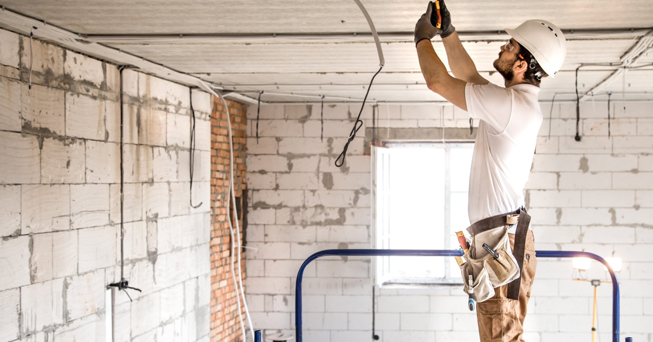 Electrician installer with a tool in his hands, working with cable on the construction site.